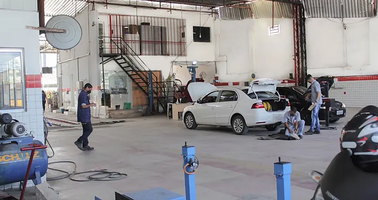 Técnicos da SIV inspecionando veículos no pátio coberto: um carro com o porta-malas aberto e o cilindro de gás à vista, e uma moto na fila