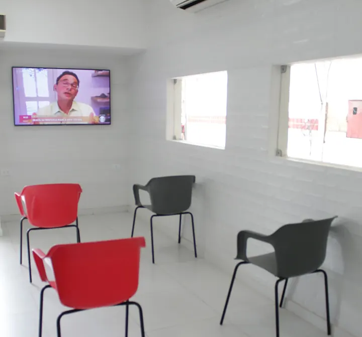 Sala de espera da SIV: parede branca, ar-condicionado ligado, televisão e cadeiras vermelhas e cinza